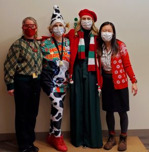 4 people wearing masks and dressed in holiday clothing and hats pose together