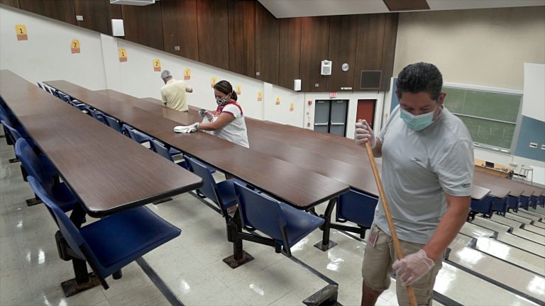 three custodians cleaning in a classroom lecture hall while wearing masks