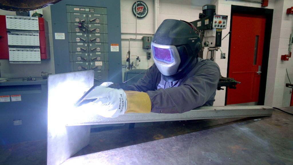 person welding wearing PPE, light sparks fly off of object