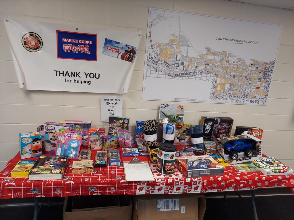toys on table with red table cloth with campus map overhead on the wall beside a "Marine Corps Toys for Tots" banner