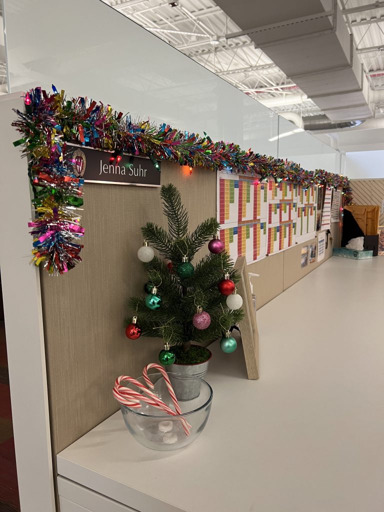 A photo of a festive workspace with small tree, candycanes, and colorful shiny garland on top of the cubicle